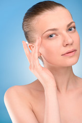 Woman applying lifting cream on face, over blue background. 