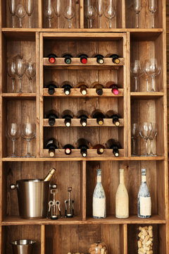 Shelving with wine bottles with glasses on wooden wall background