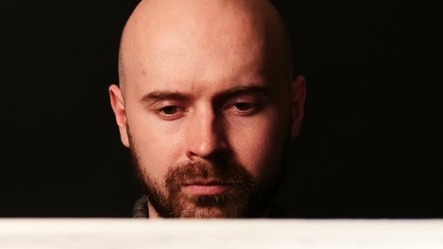 Bearded, bald artist painting something and evaluates it on