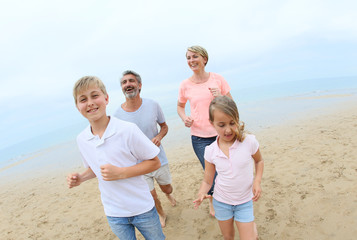 Happy family of four running on a sandy beach