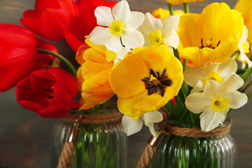 Beautiful bouquet of tulips and narcissus in glass vases, closeup