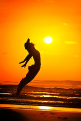 Fototapeta na wymiar young woman jumping on the beach in summer evening