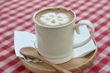 Hot cappuccino in white cup on pink tablecloth.