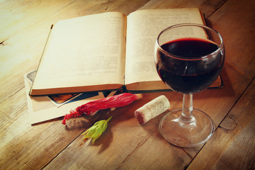 Red wine glass and old book on wooden table at sunset burst