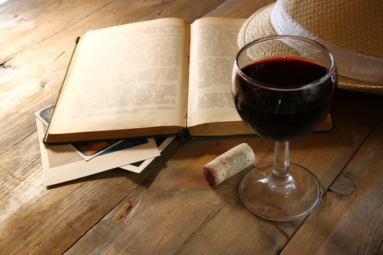 Red wine glass and old book on wooden table at sunset burst