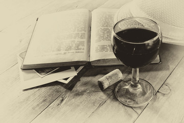 Red wine glass and old book on wooden table. vintage filtered