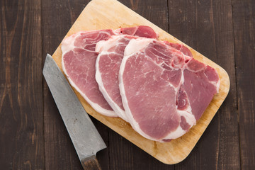 Raw pork chop steak and cleaver on wooden background