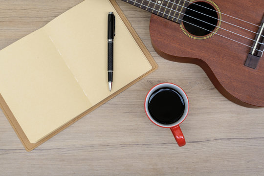 Cup of coffee with ukulele and notebook on wooden table