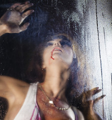Terrible and bloody woman looking through wet glass