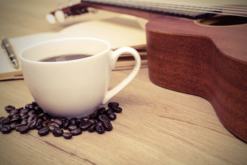 Cup of coffee with ukulele and notebook on wooden table