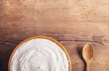 Plate with sour cream and spoon on a wooden table background