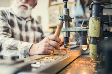 Senior man carving letters into marble plaque