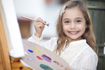 Niña de seis años sonriente pintando un cuadro en exteriores