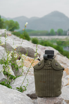Army water canteen on white rocks at riverside