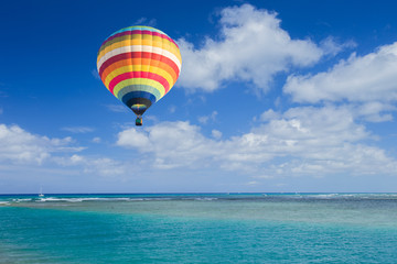 Naklejka premium Hot air balloon over ocean and clouds blue sky
