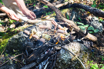 Obraz premium Cooking sausages, bread and onion on campfire during hiking