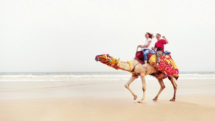 Young couple is riding a camel on the sea background.
