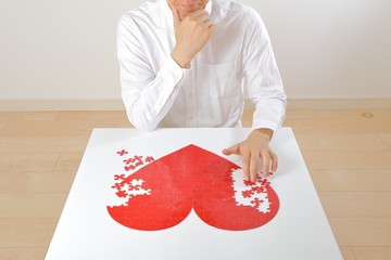 悩みながら赤いハートマークを創作している日本人男性