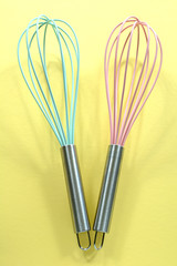 Turquoise and pink kitchen whisks on yellow background