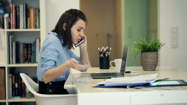 Angry businesswoman with laptop, documents talking on cellphone 