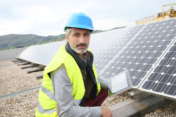 Mature engineer on building roof checking solar panels