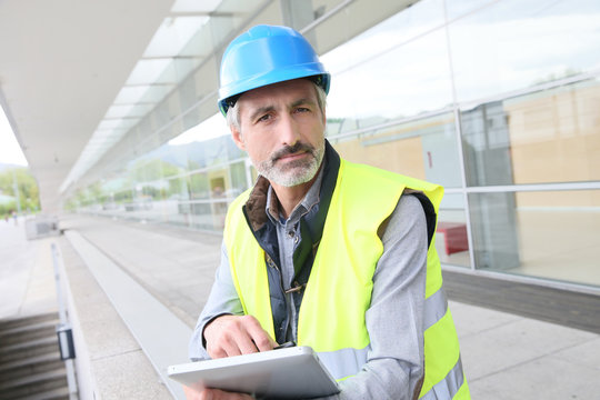 Engineer with hard hat using tablet outside building