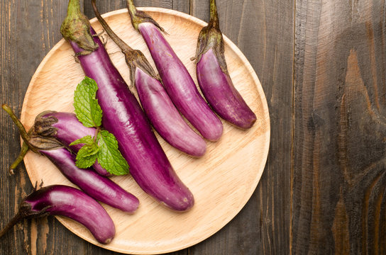 Raw eggplants on wooden plate