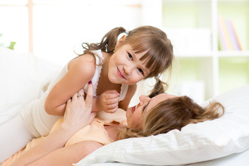 Mother and her child play and laugh in bed enjoying  sunny