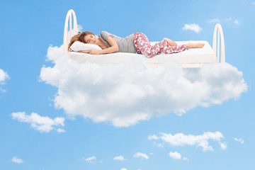 Woman sleeping on a comfortable bed in the clouds - obrazy, fototapety, plakaty