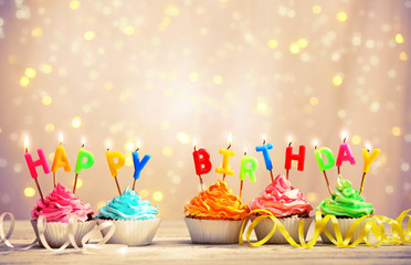 Delicious birthday cupcakes on table on light background