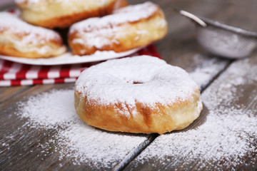 Delicious donuts with icing and powdered sugar on wooden background