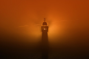 silhouette of lighthouse in fog at sunrise