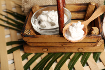 Bowl of coconut oil with leaves on wooden background