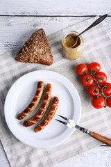 Grilled sausages on plate with bread and cherry tomatoes on table close up