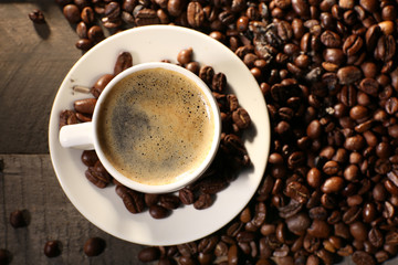 Cup of coffee with grains on wooden table, top view