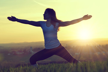 Silhouette of young woman stretching on a meadow at sunset