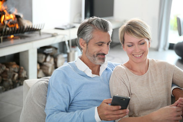 Mature couple at home having fun using smartphone