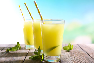 Glasses of cocktails on wooden table on bright blurred background