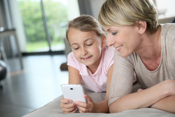 Mother and young girl playing with smartphone at home © goodluz
