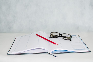 diary, glasses and a pencil on a light background