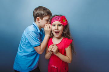 Teen boy whispering in the ear of teen girl on  a gray  backgrou