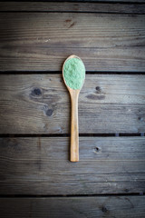 Green powder in spoon on old wooden table