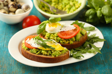 Tasty sandwiches with egg, avocado and vegetables on plate, on wooden background