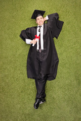 Pensive graduate holding diploma and lying in a field