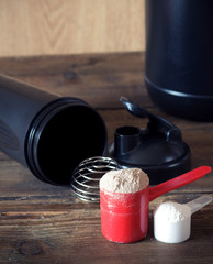 Whey protein powder in scoop with vitamins and plastic shaker