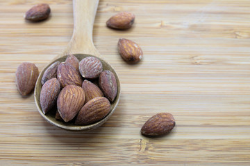 Almonds in spoon on wood background