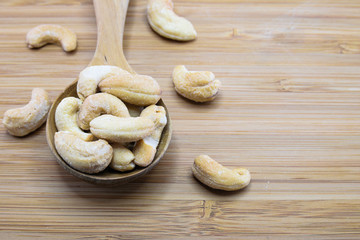 Cashews in spoon on wood background