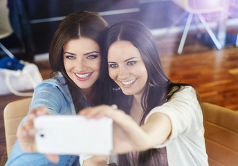 Two beautiful women taking selfie in cafe