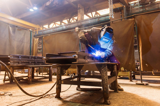 Young man with protective mask welding in a factory