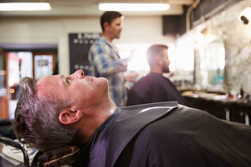 Customer Reclining In Barber's Chair Ready For Shave